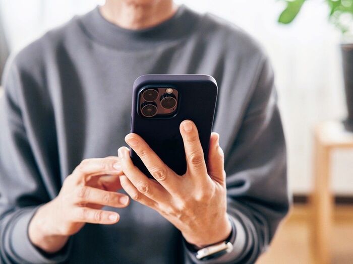 スマートフォンを操作するシニア男性。グレーのスウェットを着て、落ち着いた室内でiPhoneを使用。情報に振り回されない、ミニマルライフやデジタルデトックスを意識した暮らし。