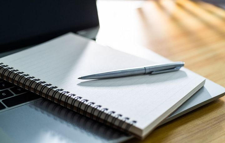 机の上のペンとスパイラルノート、ラップトップ