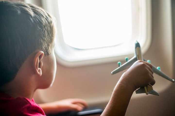 窓の外を見ながら飛行機で旅行中におもちゃの飛行機で遊んでいる少年