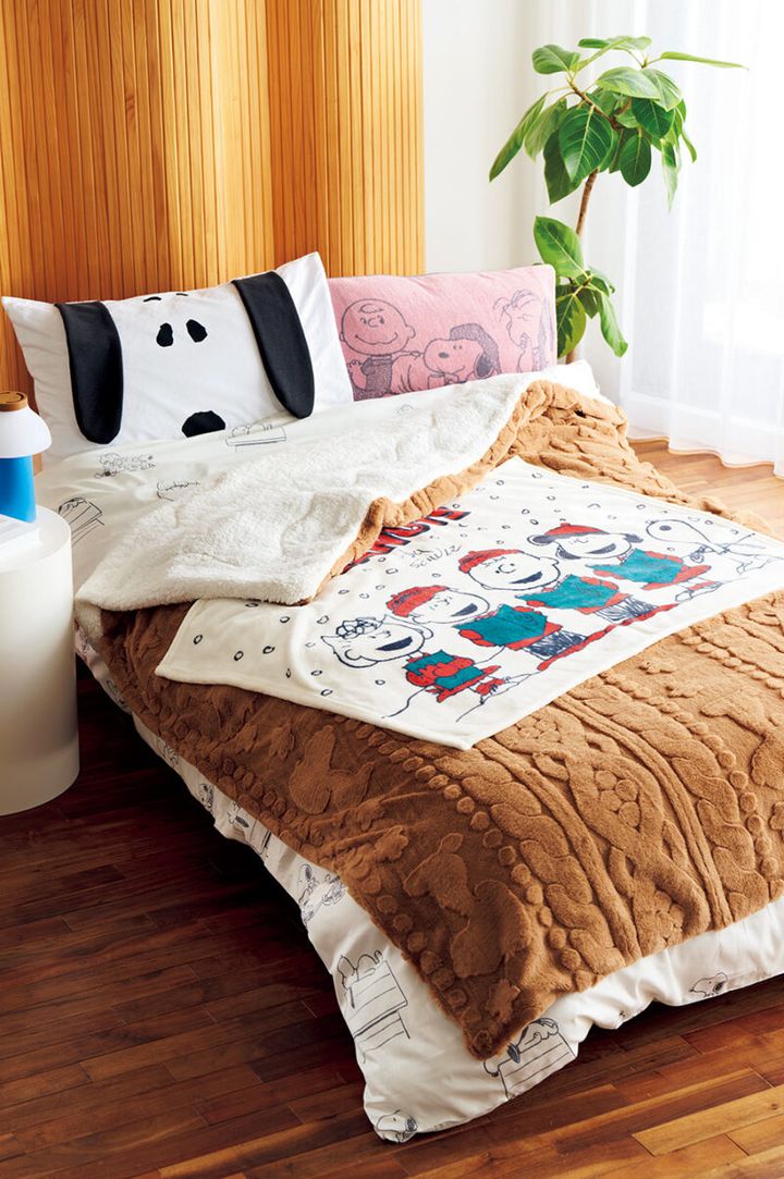 （ベッドに重ねたアイテム、下から）綿100％のサテン生地で肌ざわり滑らか。掛けふとんカバー（シングルロング：150×210cm）￥8,800。 表はスヌーピーのシルエットを織りで柄を描いた素敵なフェイクファー、裏はふんわりシープボアであったか！ キルトケット（シングル：140×200cm）¥9,900。洗えるので屋外でも使えるオケージョンひざ掛け（100×70cm）￥1, 980。（右上）のびのびタオルピローケース（約64×34cm）￥2, 200、（左上）ピローケース（65×45cm）￥2,970／すべてnishikawa