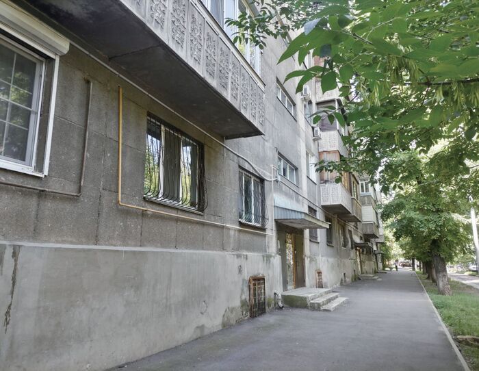 古い集合住宅が立ち並ぶ住宅街の風景。コンクリートの建物と緑の木々が並ぶ静かな通り。