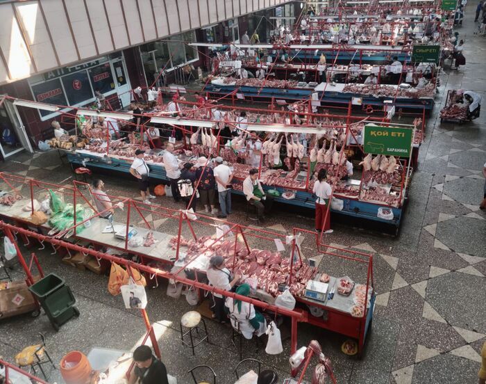 屋内市場の精肉コーナーの様子。多数の肉が吊るされ、売り手と客でにぎわっている。