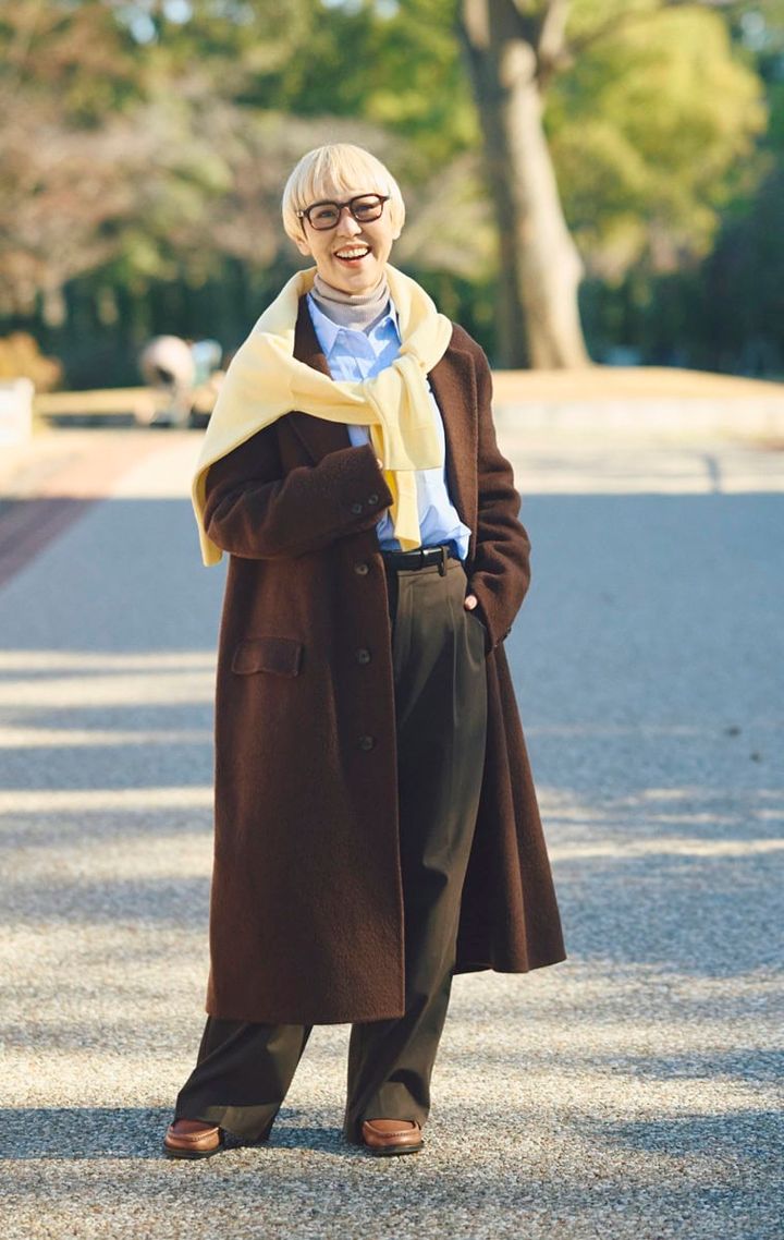 コートの上からバナナイエローのニットを肩かけ