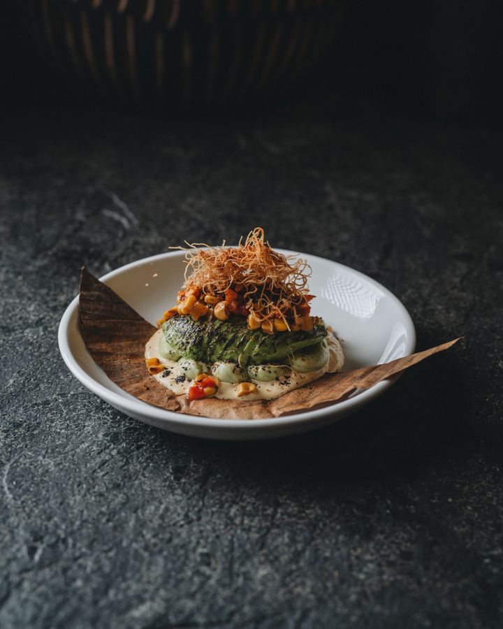 「グリルアボカド」。下には地中海と南米の要素を掛け合わせたコーン、玉ねぎ、パプリカによる燻製ピクルス風ソフリート、アジアの旨味を加える“桃屋のにんにく”（！）、クリスピーエシャロット、そしてアボカドクリームを。