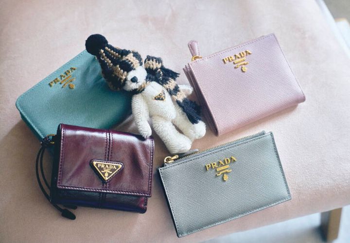 上段右から、「サフィアーノ」レザーはキズや汚れがつきにくく、長くきれいに使えるのが嬉しい。レタリングロゴとスモーキーなピンクが大人っぽくて上品。薄くてコンパクトな二つ折り。ウォレット［H8.5×W 11.5×D2、カード入れ8］￥103,400、ポンポン付きのニットキャップとマフラーを巻いたほっこりスタイルが可愛い。チャーム￥116,600、レトロシックなグリーン。使い勝手のいい二つ折り。ウォレット［H8.5×W12×D3.5、カード入れ6］￥138,600、下段右から、クールなブルーがスタイリッシュ。フラグメントケース［H8×W13、カード入れ5］￥88,000、柔らかくてなじんだレザーの質感とトライアングルロゴがかっこいい。トレンド感のあるボルドー。ウォレット［H8.5×W10×D2、カード入れ4］￥108,900（すべてプラダ／プラダ クライアントサービス）※すべて予定価格