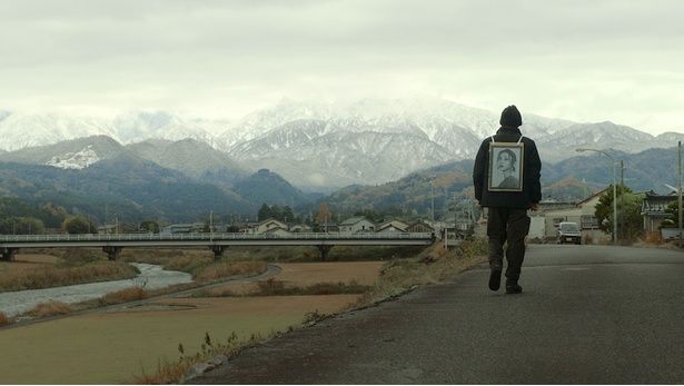 果てしなく続く山景色のなか、妻の遺影を手にさまよう信治 [c]2026 #VIRAL PRODUCTION COMMITTEE