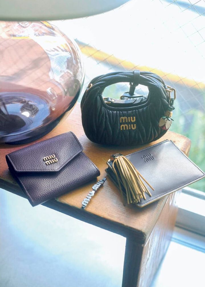上から、細部まで精巧に再現された完成度の高さ。花のチャームまで揃っていてワクワク。バッグチャーム［H9・5×W12×D5］￥161,700、バッグチャームにつけたチャーム￥31,900、ボリューミーなフリンジとロゴ入りのメタルパーツがインパクト大。後ろにカードスロット、取り外し可能なキーリング付き。カードホルダー［H8×W11、カード入れ3］￥83,600、メタルのロゴをのせたフロントフラップと、きれいなシボのボルドーカラーがクラシカルで上品。ウォレット［H8×W9×D2、カード入れ3］￥88，000、アイコニックなロゴデザイン。ヘアピン￥52,800※すべて予定価格（ミュウミュウ／ミュウミュウ クライアントサービス）