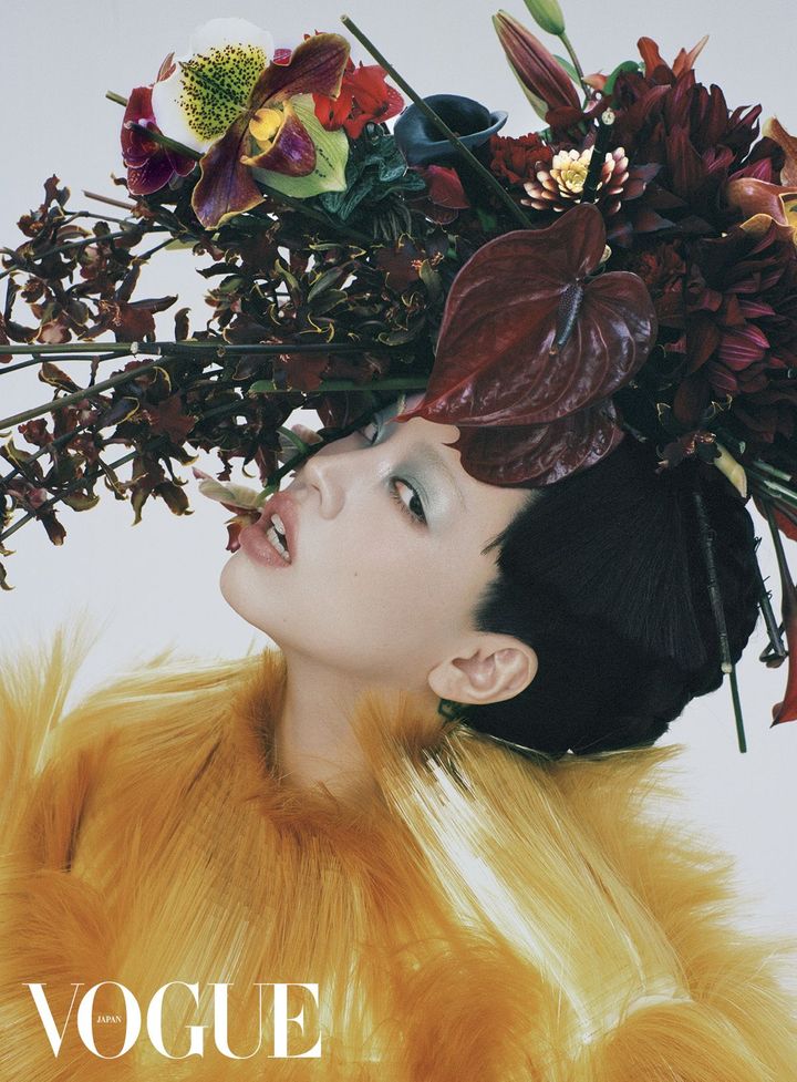 生けるものの艶やかな輝き 日本と縁の深い“赤”という色。一口に言ってもその色調はさまざまだが、今回ヘッドピースを手がけたフラワーアーティストの東信は、ちゃんみなとVOGUEの撮影にあたり、よりモードで、内面の強さを引き出す深い赤を選んだ。「このヘッドピースだけでも、30種類ほどの花を使っています。いわゆる和の飾りはまったく入れていませんが、流れや形式、そして生ける人の気持ちによって、仕上がりは力強く、日本らしくなったと思います。同じ植生では咲かない花をこうやって出会わせて、一つ一つの命を預かって、作品を作り上げる。その完成形が、見事にちゃんみなさんと合致したと感じました」。金色のトップ、生き生きとした生命の息吹を宿す花、そしてちゃんみなが持つ感性が混ざり合い、強烈なエネルギーを放つ。<br /> コート ￥4,202,000／BOTTEGA VENETA（ボッテガ・ヴェネタ ジャパン）