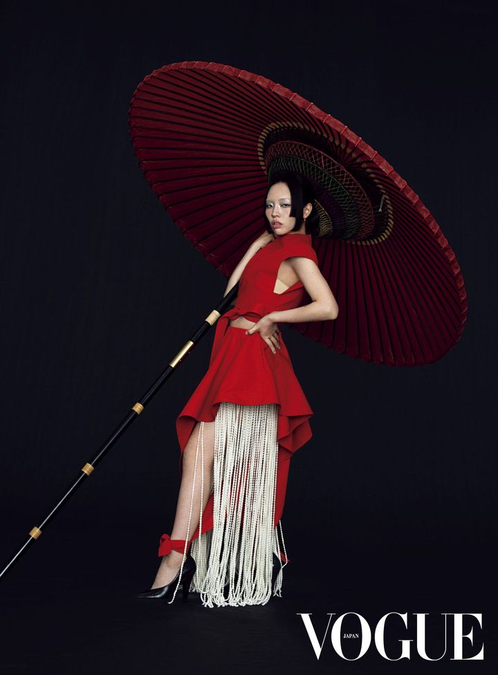 赤と白、そこに生まれる美学 アライアの2026年春夏コレクションの着想源は、日本。ブランドを象徴するシャープなカッティングと、美しく揺れるフリンジを、赤と白の配色で描いたドレスが、東洋的な緊張感を纏う。漆黒の空間に、野点傘を携えてしなやかに佇むその姿は、伝統とモダンが静かに交わる瞬間を印象づける。<br /> トップ ￥236,500 パンツ ￥294,800 フリンジニットパンツ ￥629,200（参考価格） シューズ ￥269,500（参考価格）／すべてALAÏA（リシュモン ジャパン アライア） イヤリング「クラッシュ ドゥ カルティエ」 PG×レッドアゲート ￥1,557,600／CARTIER（カルティエカスタマー サービスセンター）