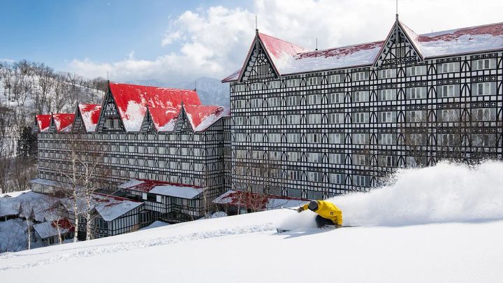 赤屋根のホテルを背景に雪煙を上げて滑るスキーヤー