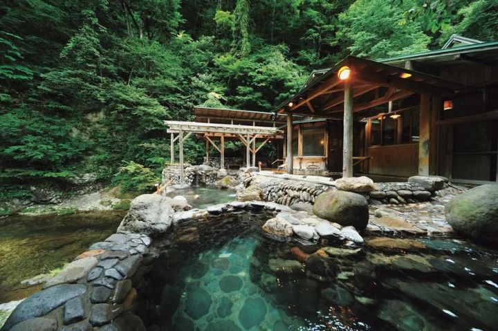 渓流沿いの露天風呂と木造湯屋が写る一の坊リゾートの温泉風景