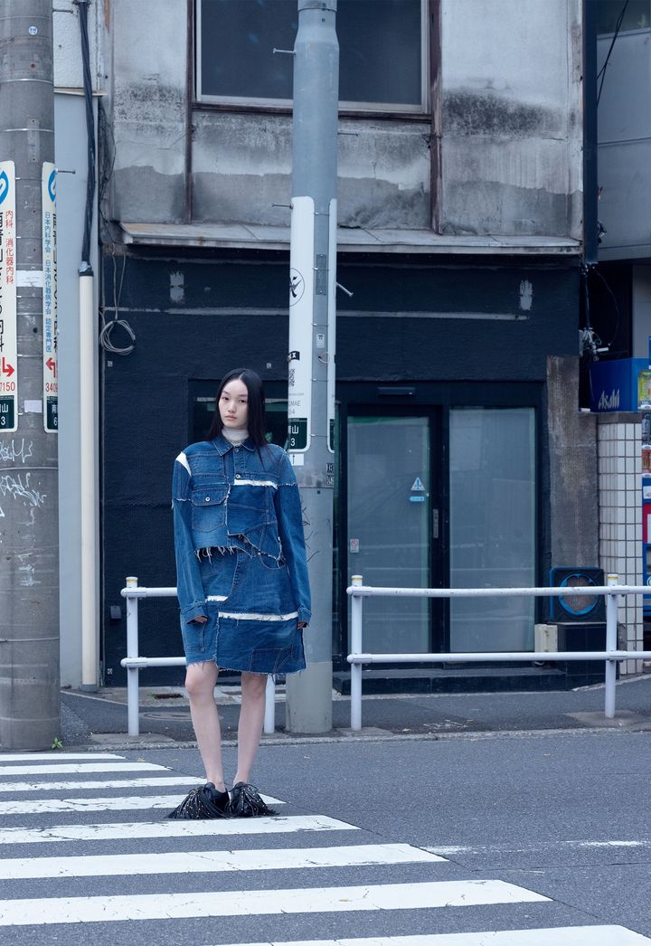 テクニックを進化させ、サカイらしさを突きつめる <br /> 青山にあるサカイの本社前の交差点で、写真家ホンマタカシが捉えた「自分らしく生きるサカイウーマン」たち。「Coming Home」をテーマに、「紛れもなく、疑いようもないサカイ」を表現した2026年春夏は、デザイナーの阿部千登勢自らが、サカイらしさを改めて見つめ直し進化させたコレクション。「今着たい服」というリアリティを持ちながら、タイムレスな魅力を放っている。現代人のワードローブに欠かせないデニムも、ハイブリッドなレイヤーを重ねモダンな一着に。パッチワークデニムジャケット ￥187,000 パッチワークデニムスカート ￥154,000 スカーフネックレス ￥63,800 シューズ 参考商品