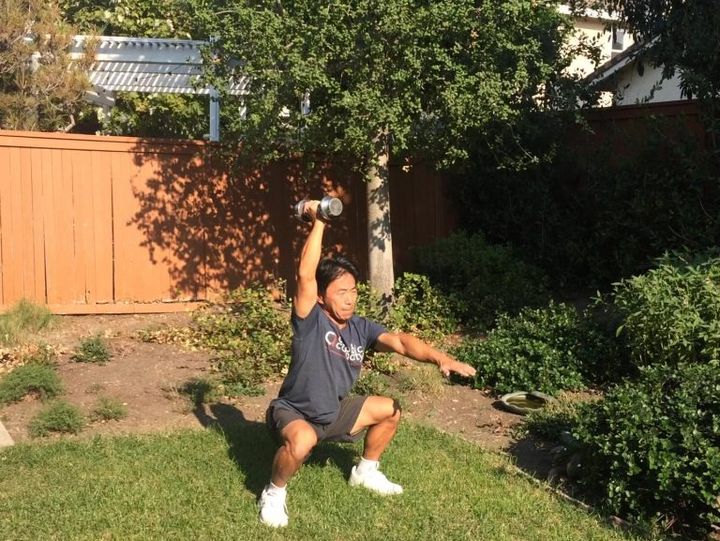 片腕オーバーヘッド・スクワット 片手を前に出し、もう片手にダンベルを持ってスクワット