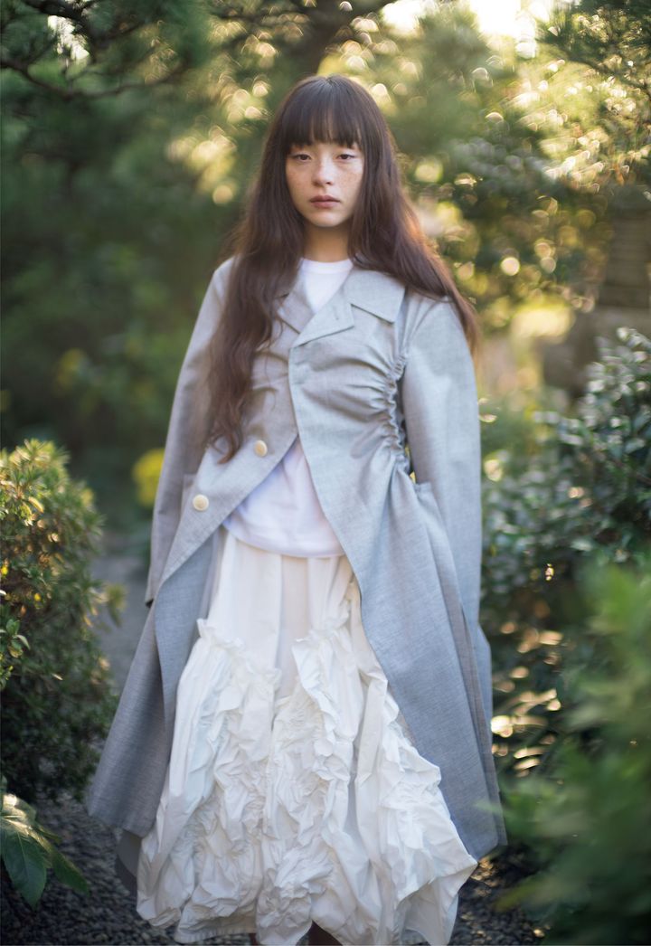 「ただそこに在る」かのような、自然体の美しさ <br /> 「今回はタオ本来のスタイル──そして私自身に忠実なコレクションを作ることに集中しました」とコレクションについて語った栗原。意外な場所にギャザーを寄せたグレイのウールコートや、花びらを思わせるシワ加工が有機的なボリュームを生み出すエステルスカート。即興のようなラフさも漂う甘すぎないディテールが、ベーシックなデザインの中にタオらしい独自のリズムを吹き込む。コート ￥214,500 Tシャツ ￥8,800 スカート￥129,800╱すべてTAO（コム デ ギャルソン）