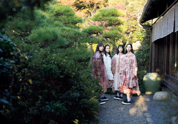 そよ風に揺れる、自由を愛する赤い花々 <br /> 穏やかな海の波音が心地よく響く、葉山の高台にある写真家・上田義彦の邸宅で行われた今回の撮影。清らかな朝日に照らされた庭で4人のモデルがまとったのは、2026年春夏コレクションの中でも特別な存在感を放ったアーティスト・今村文の作品をプリントに用いたルック。植物をモチーフにした独自の世界観で知られる今村が描くたおやかな「花々」を通し、栗原たおが追求し続ける「強さ」と「優しさ」が開花する。「今村文さんの絵は、花だけでなく根っこを描くのが特徴で、生命の根幹、生命力の強さを感じます。それを身にまとうことで、ポジティブでハッピーな気持ちになれたらと思いました」（栗原）〈左〉ワンピース ￥107,800 中に着たTシャツ ￥8,800 ジャンパースカート ￥77,000 ソックス ￥3,960 シューズ ￥68,200 〈中央左〉ジャケット ￥126,500 スカート ￥121,000 ソックス ￥3,960 シューズ ￥68,200 〈中央右〉ブラウス ￥118,800 中に着たTシャツ￥8,800 ジャンパースカート ￥77,000 ソックス ￥3,960 シューズ ￥68,200 〈右〉コート ￥170,500 中に着たTシャツ ￥8,800 パンツ 参考商品 ソックス ￥3,960 シューズ ￥68,200╱すべてTAO（コム デ ギャルソン）