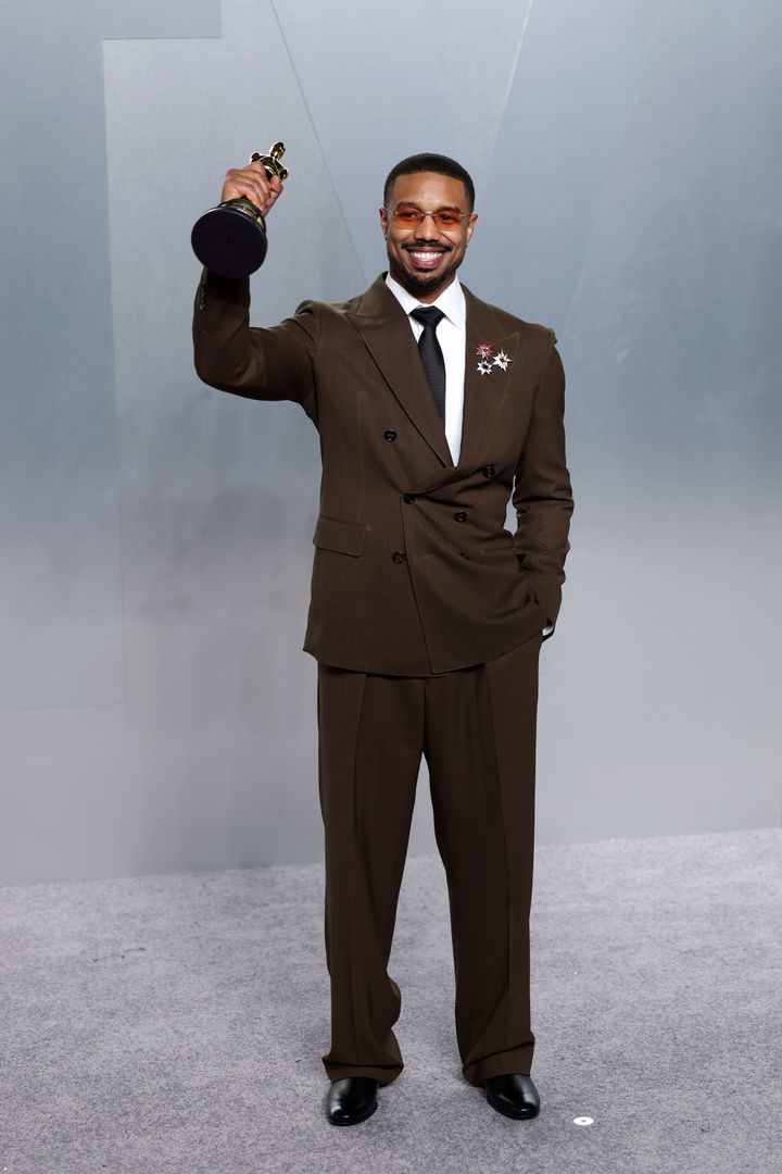 Image may contain_ Michael B. Jordan, Clothing, Formal Wear, Suit, Blazer, Coat, Jacket, Head, Person, Face, Firearm, and Gun