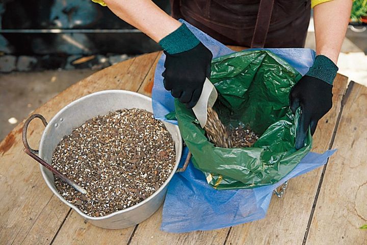 バスケットに不織布を敷き、水抜き穴を6カ所あけたビニール袋を重ね、緩効性肥料を混ぜた培養土を入れる。