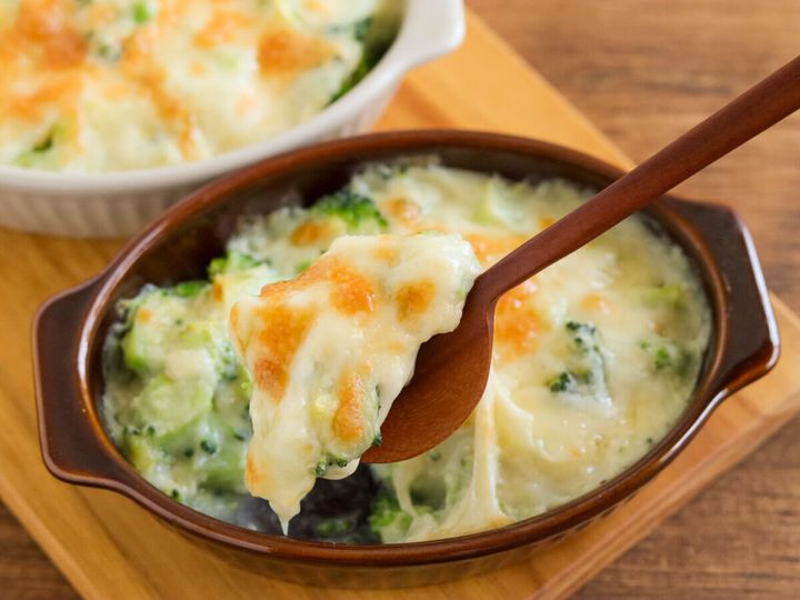 茶色のグラタン皿のブロッコリーグラタンを木のスプーンですくいチーズがとろりと伸びている様子