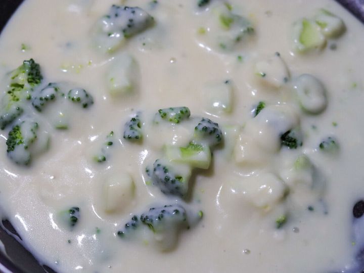 フライパンでブロッコリーが白いクリームソースに絡まって煮えている様子