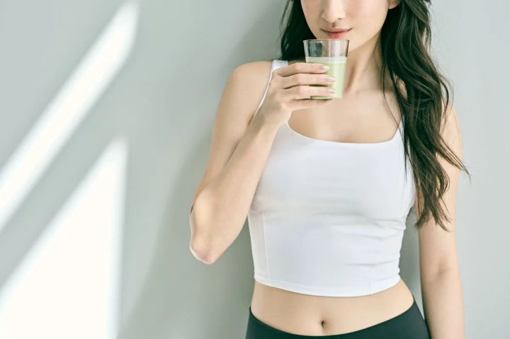 抹茶色のプロテインドリンクをグラスで飲む女性の使用