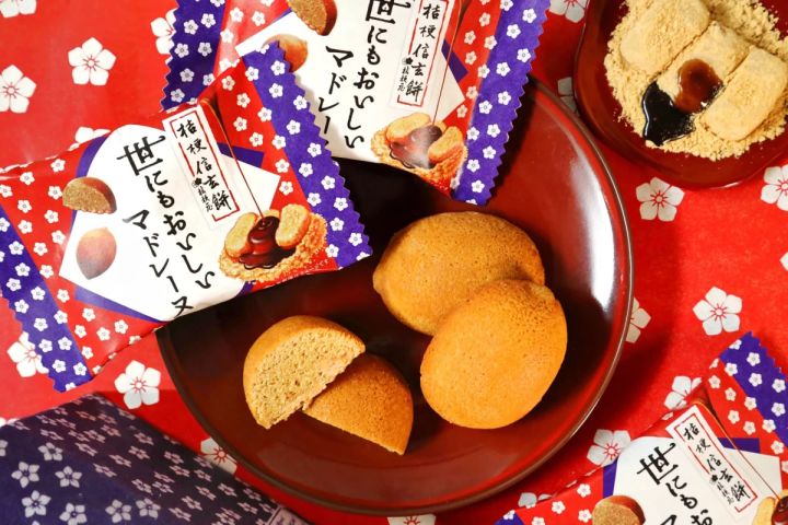 桔梗信玄餅マドレーヌが赤いうつわに盛られ、個包装も見える。背景にはきな粉と黒蜜がかかった信玄餅も写っており、赤い布地の梅柄が華やかさを添えている。