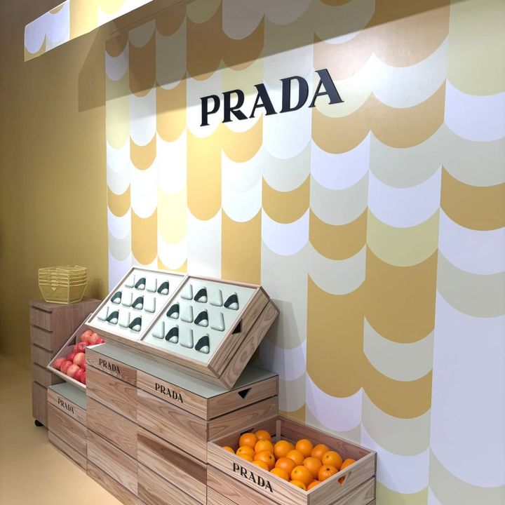 「プラダ ビューティ マーケット」のラッキードローゲーム（抽選）コーナ―。木箱に入ったリンゴやオレンジ、三角形のコスメが市場のように並ぶ様子