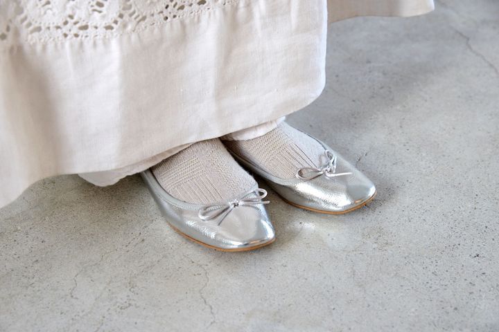 白の装いに映えるシルバーのバレエシューズとソックスを合わせた軽やかな足もと