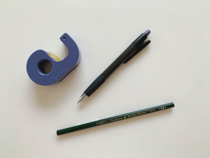 白い机の上に置かれたテープカッターとシャープペンシルと鉛筆