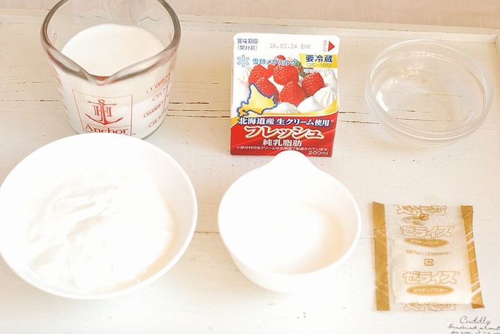 パンナコッタの材料（牛乳、生クリームパック、ヨーグルト、砂糖、粉ゼラチン）を白いテーブルに並べた写真