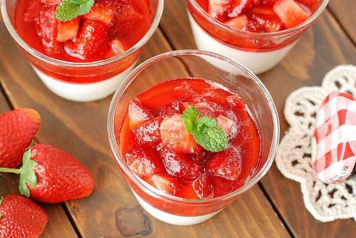 グラスに入ったパンナコッタに角切りいちごソースとミントの葉をのせた完成品3つを木製テーブルに並べた俯瞰写真