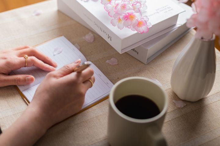 日本の春の桜の花をテーブルに飾ってノートにメモをする女性の手元