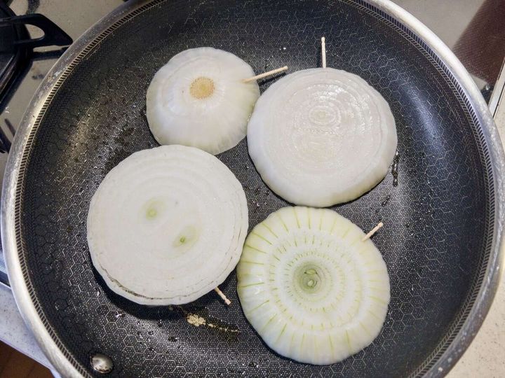 フライパンに爪楊枝を刺した輪切り新玉ねぎ4枚を並べてオリーブオイルで焼いている俯瞰写真