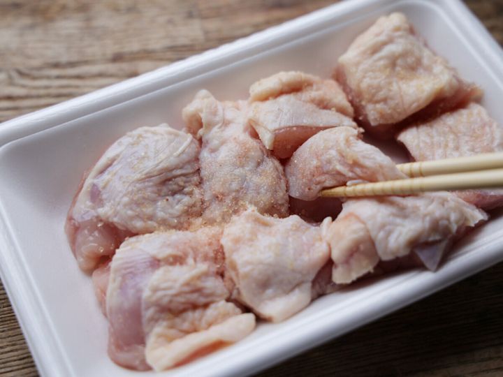 白いトレーのひと口大鶏もも肉に塩と砂糖をふって箸でなじませている下準備の写真