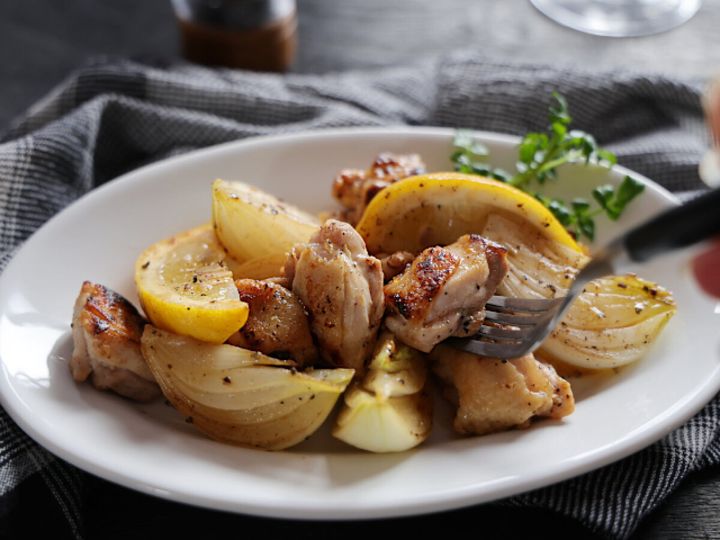 白い丸皿に鶏もも肉と新玉ねぎのレモンペッパー炒めを盛りフォークを差したクレソン添えの完成品