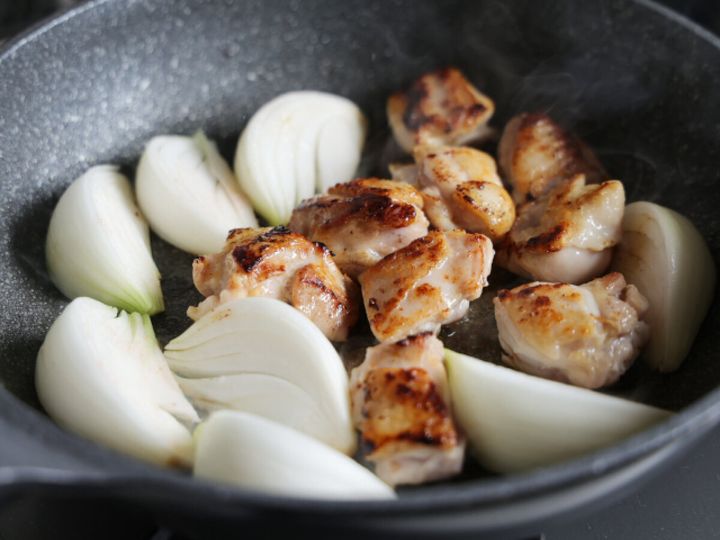 フライパンで焼き色のついた鶏もも肉を裏返し新玉ねぎのくし切りを加えた工程の写真