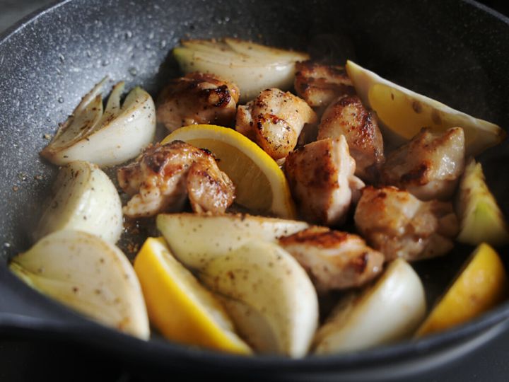 フライパンの鶏もも肉と新玉ねぎにレモンを加え粗挽き黒こしょうを振って混ぜている工程の写真