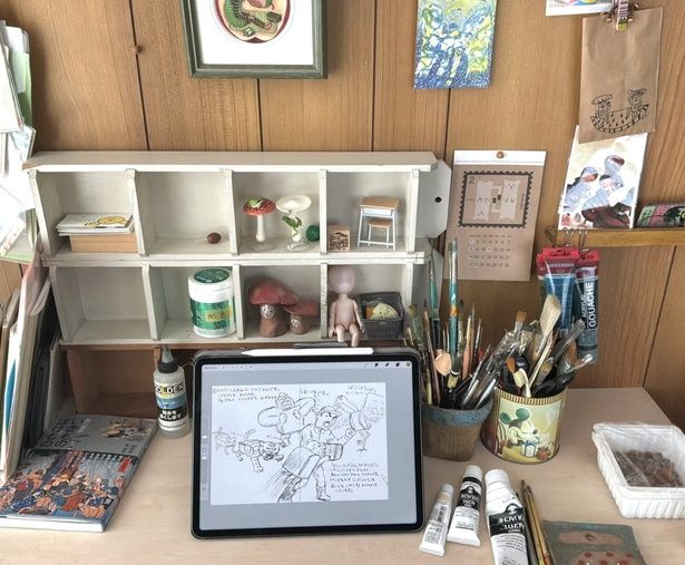 作業場の様子。息子のお古の学習机にベニヤ板を置き、面積を広くして使っています。ラフや見返しの線画は、iPadで描いています