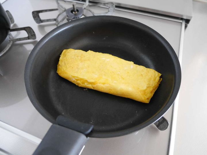 ガスコンロの上の黒い丸いフライパンで卵焼きを焼いている様子