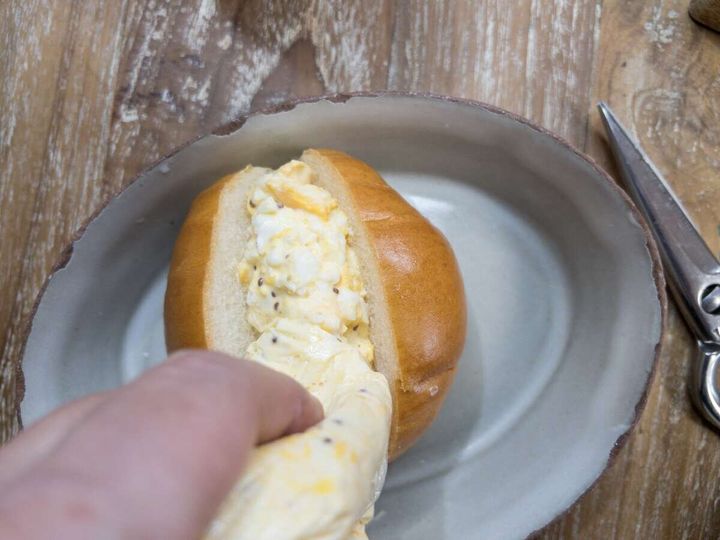 端を切ったアイラップからロールパンの切り込みに卵サラダを絞り出している工程写真