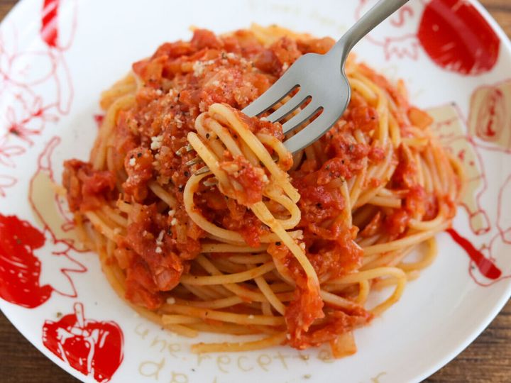 トマト柄の白い皿に盛ったツナトマトパスタにフォークを差した完成品の斜め俯瞰写真