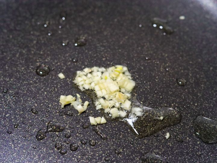 フライパンにオリーブオイルとみじん切りにんにくを入れ弱火で加熱している工程のクローズアップ写真