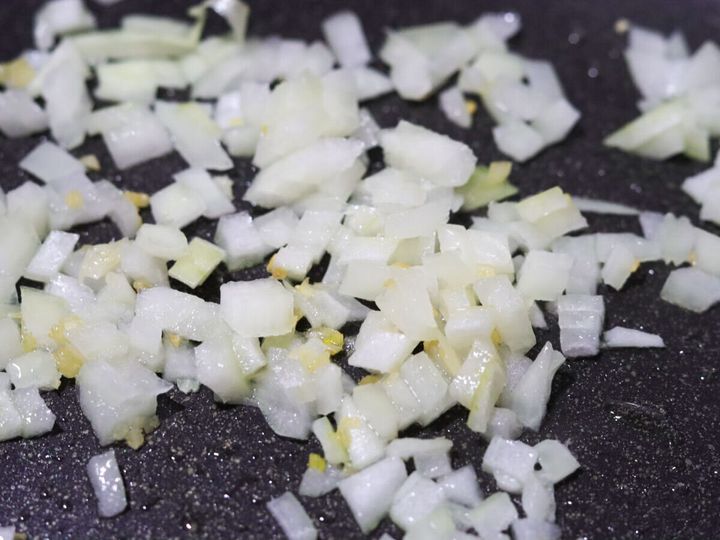 フライパンでにんにくと一緒にたまねぎをしんなりするまで中火で炒めている工程のクローズアップ写真