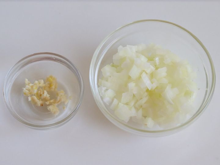 みじん切りのにんにくと粗みじん切りのたまねぎをそれぞれガラスボウルに入れた下準備の俯瞰写真
