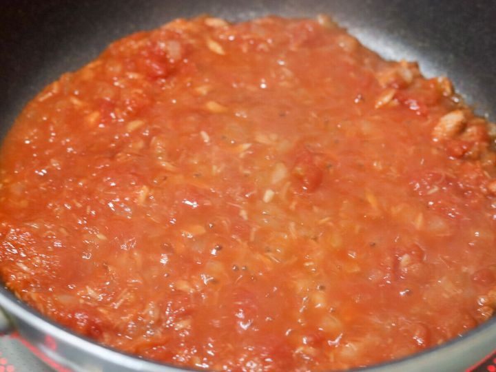 フライパンのツナトマトソースに砂糖とゆで汁を加え唐辛子を入れてさらに煮詰めている工程写真