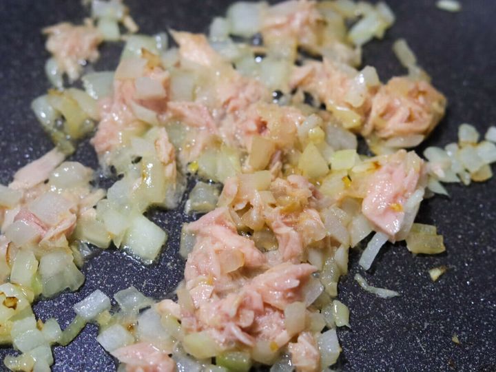 フライパンのたまねぎとにんにくにツナ缶を汁ごと加えてさっと炒めている工程のクローズアップ写真