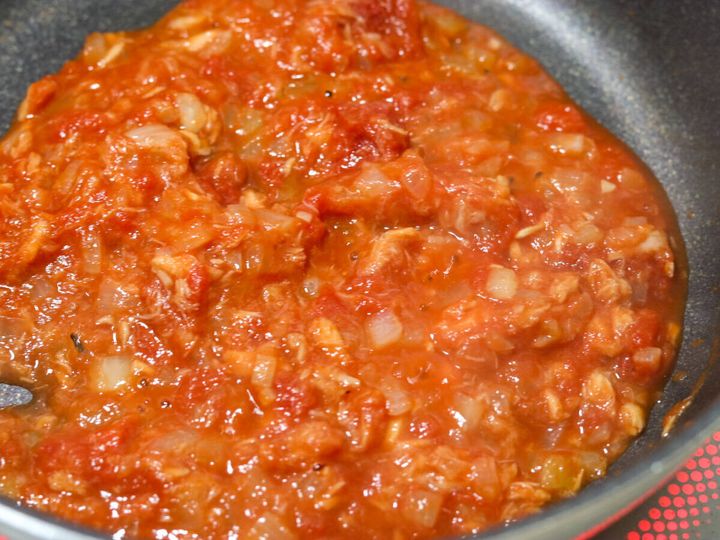 フライパンでホールトマト缶を加えてツナとたまねぎと炒め合わせ中火で煮詰めているトマトソースの工程写真