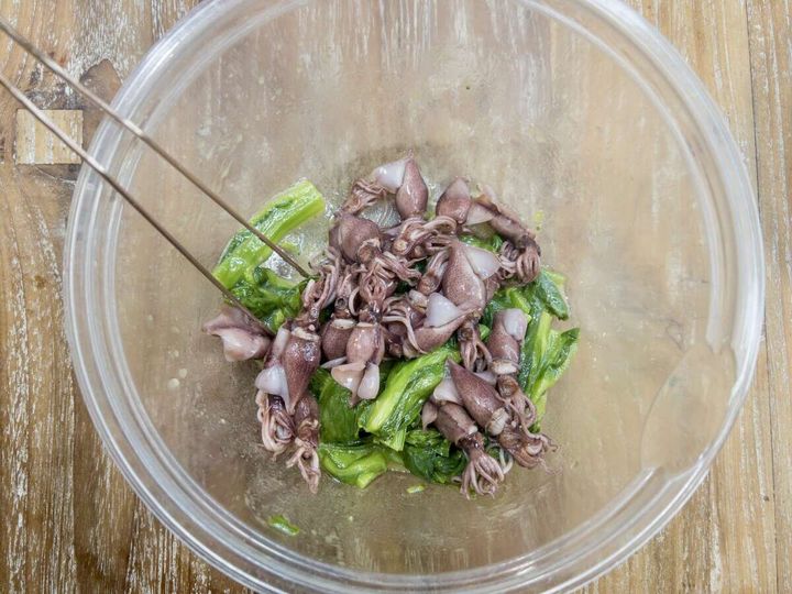 ガラスボウルで菜の花とホタルイカをトングでマリネ液と和えている工程の俯瞰写真