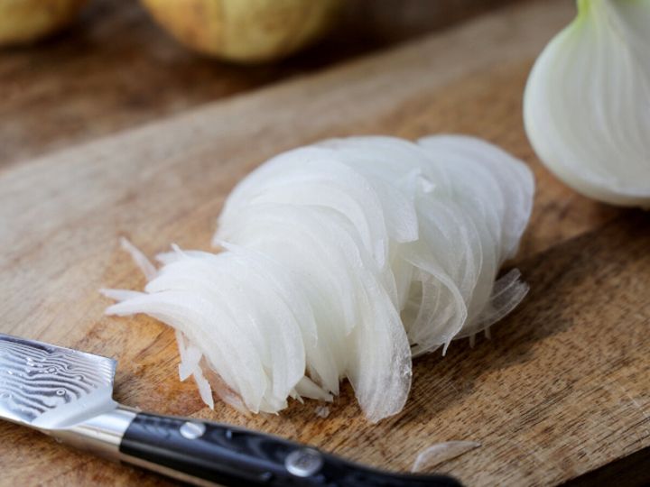 木のまな板の上で繊維に沿って薄くスライスした新玉ねぎ