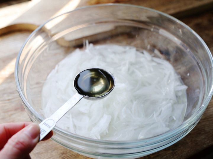 ガラスボウルの酢水に浸けた新玉ねぎスライスに計量スプーンで酢を加える様子