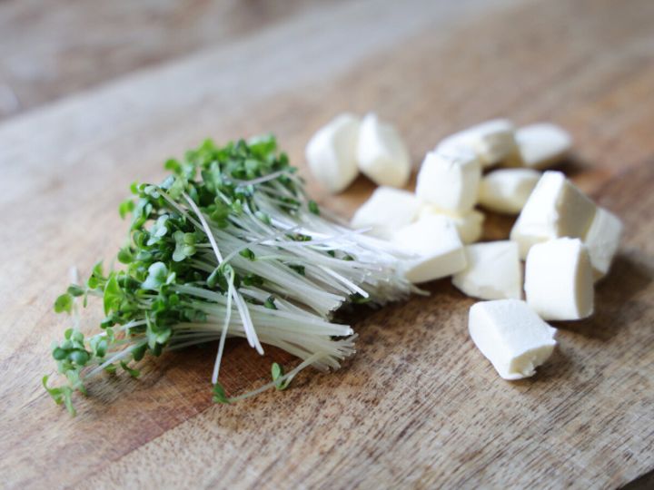 まな板の上に並べたブロッコリースプラウトと角切りのクリームチーズ